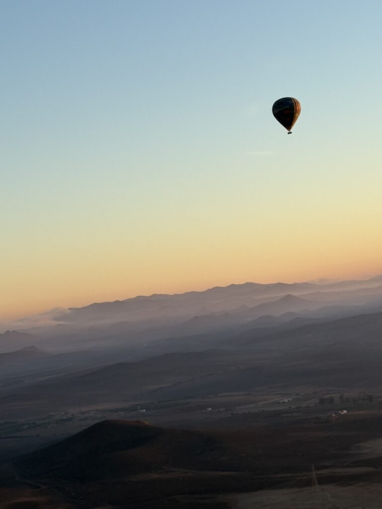 View of a hot air balloon in flight at sunrise, with the Atlas Mountains in the background. 